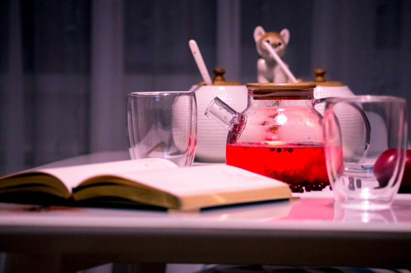 An open notebook sits beside a glass teapot and teacups.